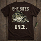 Brown t-shirt with graphic of a bass eating a smaller fish and text "SHE BITES ONCE."
