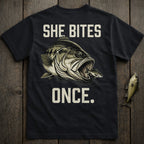 Black t-shirt with "SHE BITES ONCE." and a graphic of a bass eating a smaller fish.