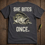 Dark t-shirt with a large bass eating a smaller fish and text "SHE BITES ONCE."